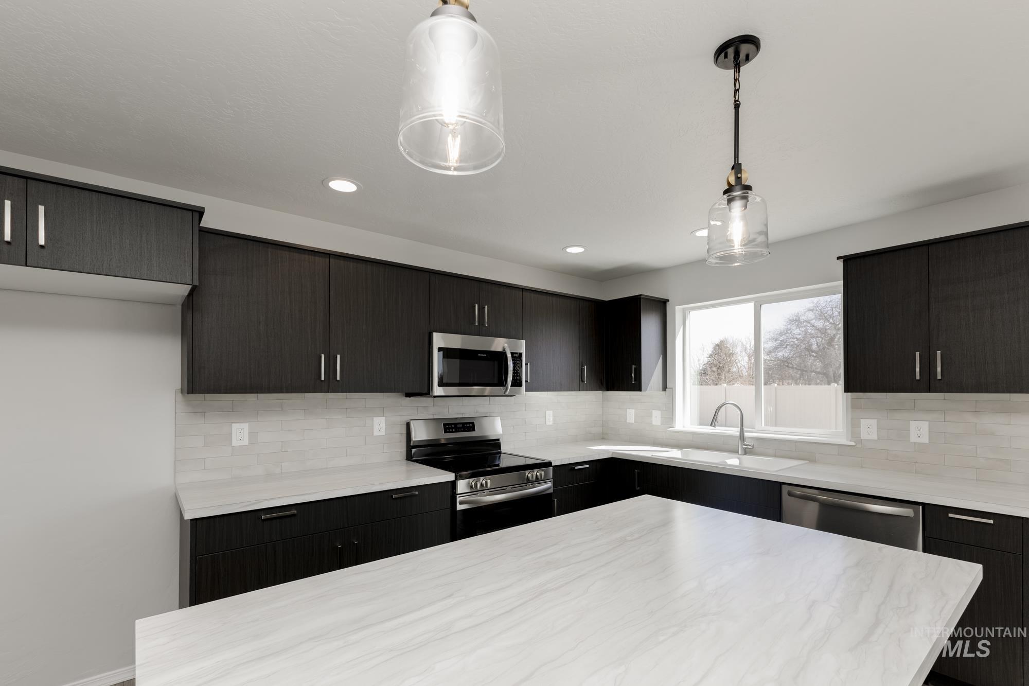 3270 South Maple Rnch Way Nampa, ID 83686 - Photo 6 of 31 Kitchen with appliances with stainless steel finishes, hanging light fixtures, backsplash, a kitchen island, and modern cabinets