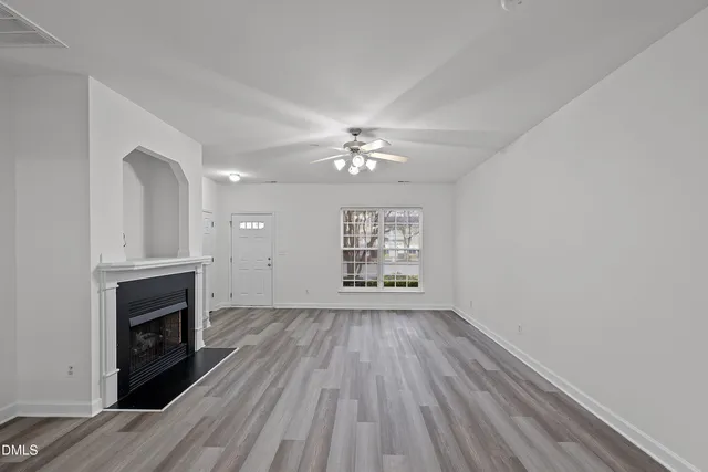 a view of an empty room with wooden floor fireplace and a window