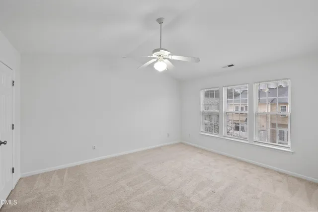 an empty room with chandelier fan and windows