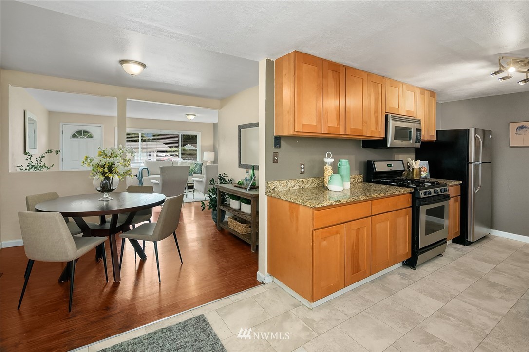 2613 Northeast 7th Street Renton, WA 98056 - Photo 10 of 23 a kitchen with stainless steel appliances granite countertop a stove a sink dishwasher a dining table and chairs with wooden floor