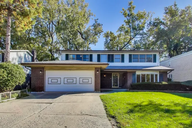a view of a house with a yard plants and large tree