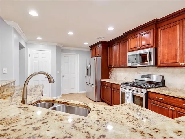 a kitchen with stainless steel appliances granite countertop a stove a sink dishwasher a refrigerator and wooden cabinets with wooden floors