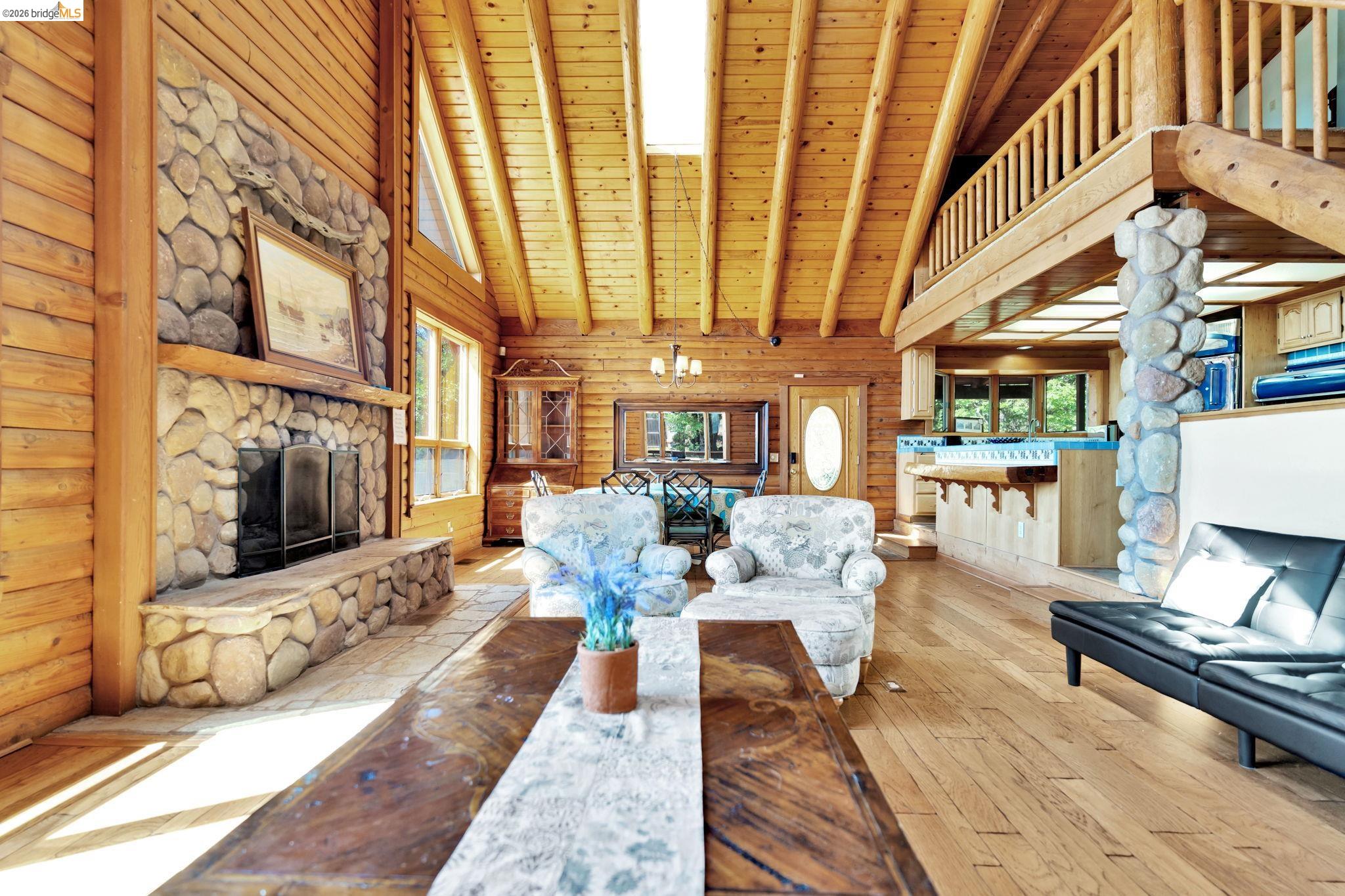 14799 Big Hill Road Sonora, CA 95370 - Photo 12 of 60 Living area featuring a fireplace, light wood-style floors, a high wood beamed ceiling, suspended lighting, and wooden walls