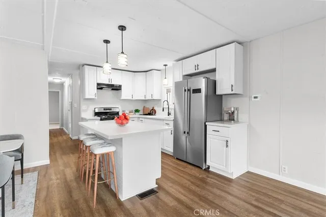 a kitchen with stainless steel appliances a refrigerator a stove a sink dishwasher a stove and white cabinets with wooden floor