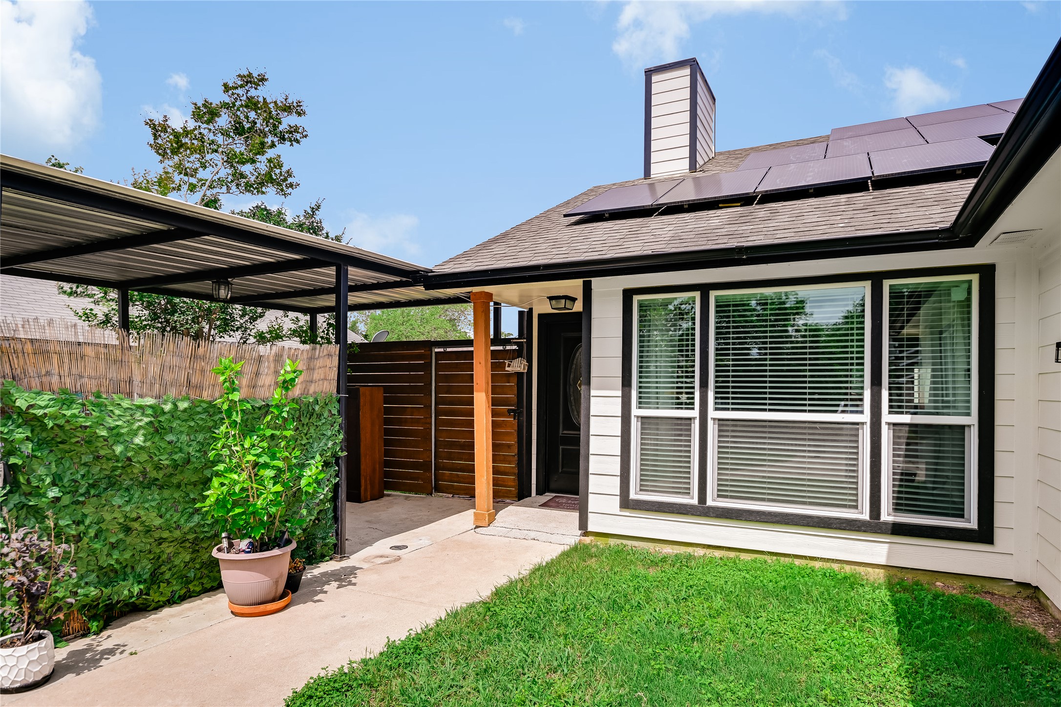 4702 Crest Oak Road Austin, TX 78744 - Photo 2 of 20 Contemporary exterior featuring white siding with black trim, a covered carport, and a prominent front entrance