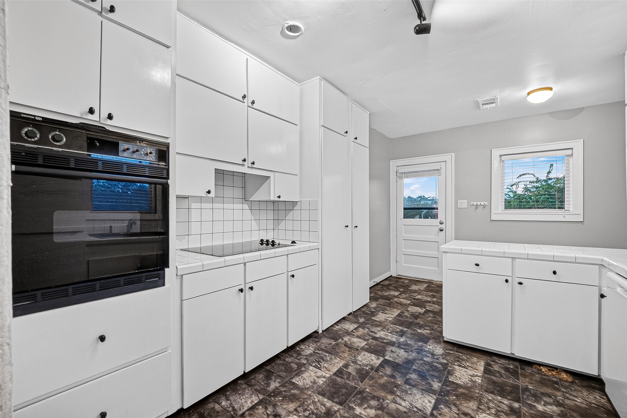 1758 Hawthorne Street, Unit 2 Houston, TX 77098 - Photo 6 of 19 This kitchen features a modern design with white cabinetry, dark countertops, and a stylish tile backsplash. It includes ample storage, a built-in microwave, and under-cabinet lighting. The space is bright and functional, with a window and door leading outside.