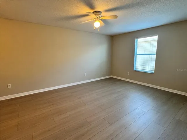an empty room with wooden floor and fan