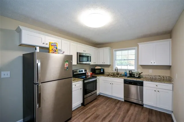 a kitchen with a refrigerator a sink dishwasher a stove and white cabinets with wooden floor