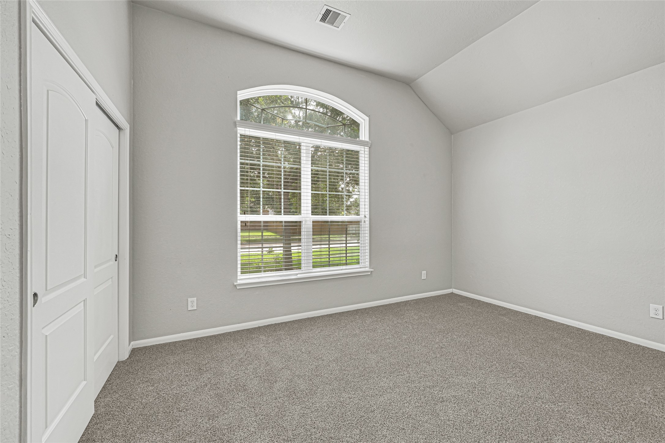 4702 Sedgewood Drive Rosenberg, TX 77471 - Photo 6 of 24 This room features a spacious, light-filled area with neutral walls and carpet. It has a large arched window offering a view of the greenery outside, and a closet with sliding doors, ideal for a bedroom or office space.