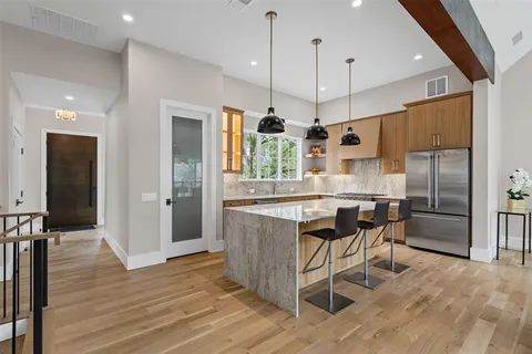a kitchen with stainless steel appliances granite countertop a kitchen island a stove a refrigerator a sink a dining table and chairs with wooden floor