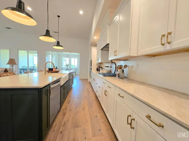 a kitchen with stainless steel appliances a sink dishwasher a refrigerator and white cabinets with wooden floor