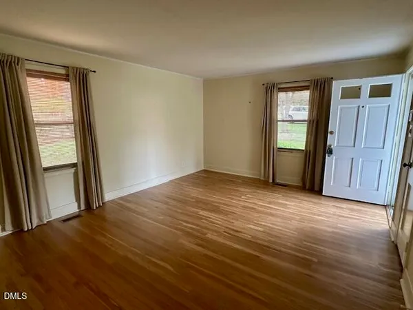 a view of an empty room with window and wooden floor
