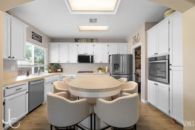 a kitchen with stainless steel appliances granite countertop a stove a sink a refrigerator white cabinets and wooden floor