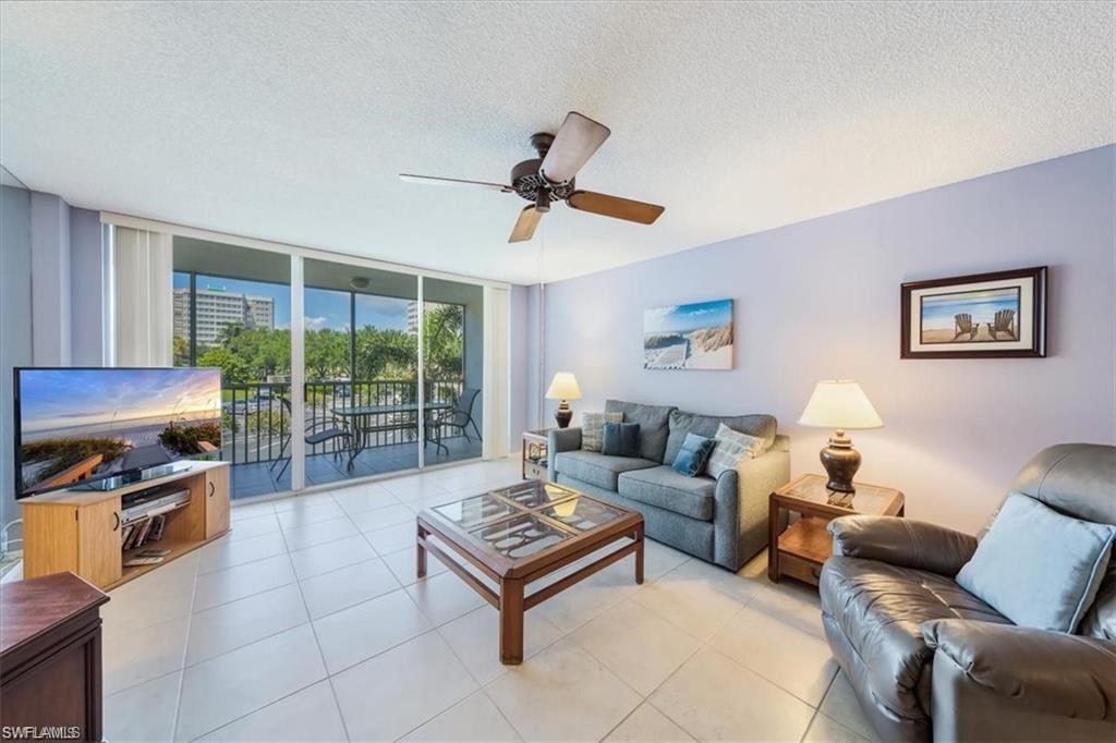 3 Bluebill Avenue, Unit 207 Naples, FL 34108 - Photo 7 of 32 a living room with furniture a flat screen tv and a floor to ceiling window