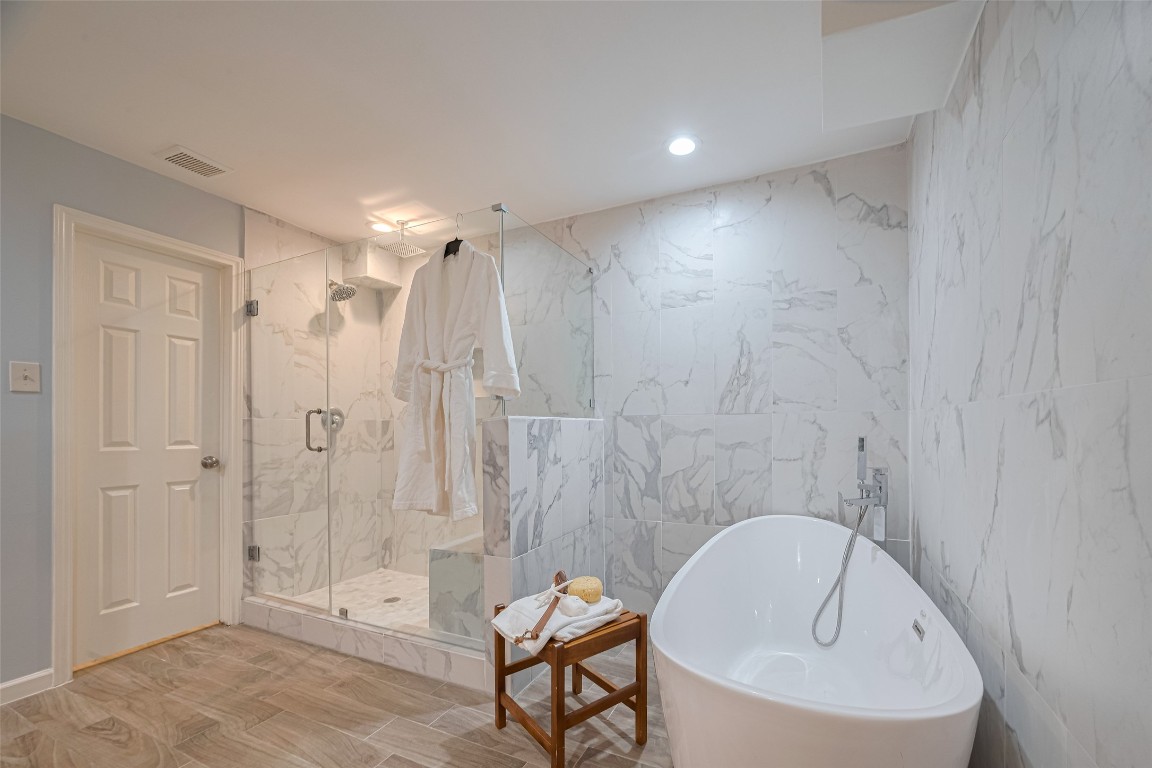 15600 Barkers Landing Road, Unit 20 Houston, TX 77079 - Photo 34 of 49 This modern bathroom features a luxurious freestanding bathtub and a spacious glass-enclosed shower, with elegant marble like tile throughout and warm wood-style tile flooring.