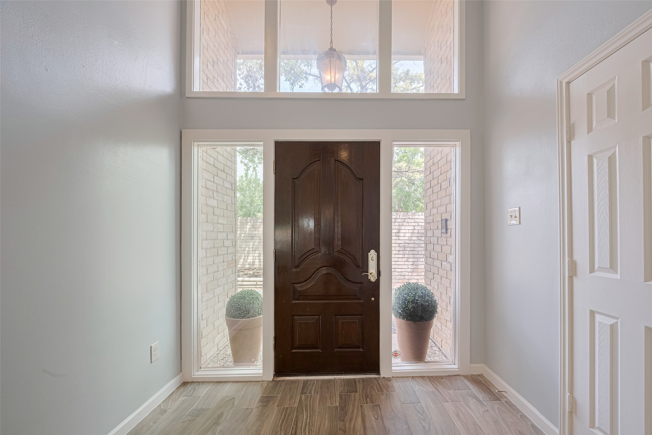 15600 Barkers Landing Road, Unit 20 Houston, TX 77079 - Photo 3 of 49 This entryway features a dark wooden front door flanked by large sidelights, offering plenty of natural light. The space has light-colored walls, wood-look flooring, and a high ceiling with transom windows above, creating an inviting and airy atmosphere.