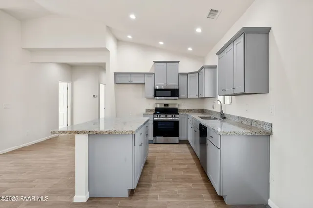 a kitchen with stainless steel appliances granite countertop a stove top oven a sink and white cabinets