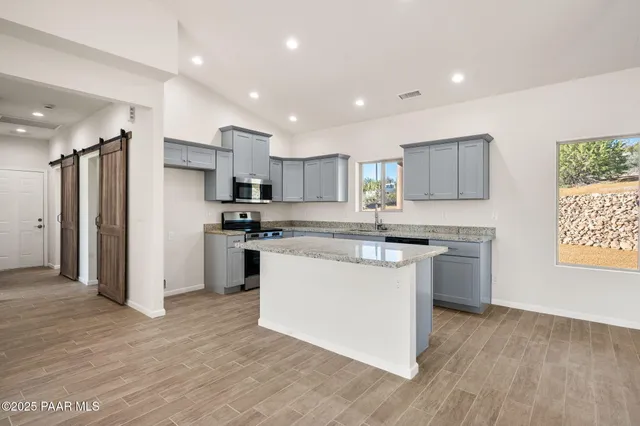 a kitchen with stainless steel appliances granite countertop a refrigerator a sink dishwasher a stove and white cabinets with wooden floor