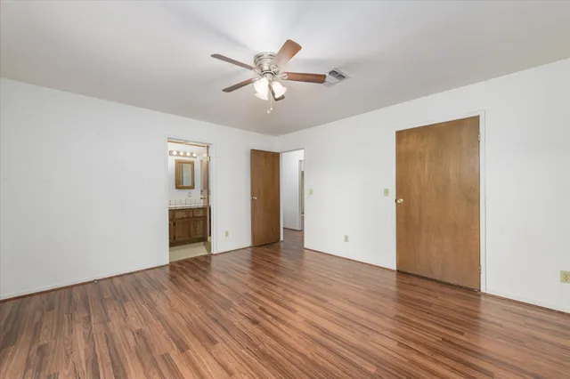a view of an empty room with wooden floor and a ceiling fan