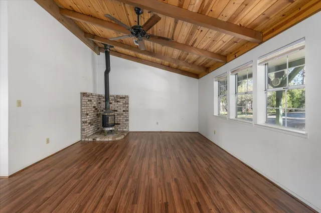 a view of an empty room with wooden floor a ceiling fan and windows