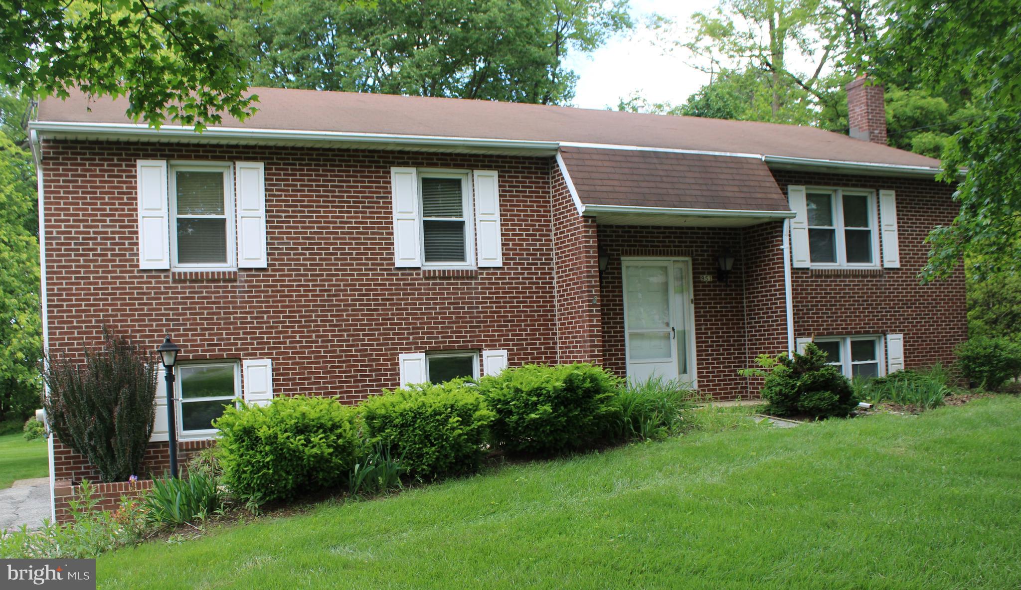 a view of a house with a yard plants and large tree