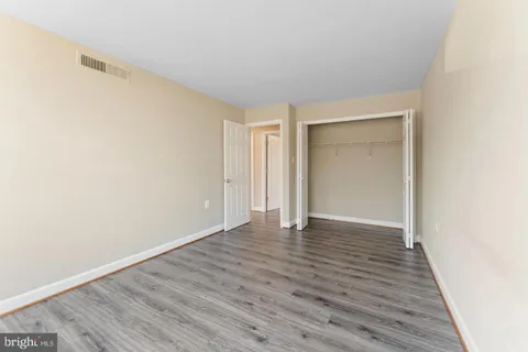 a view of an empty room with wooden floor and closet