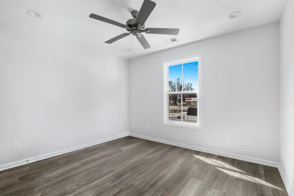 an empty room with wooden floor ceiling fan and windows