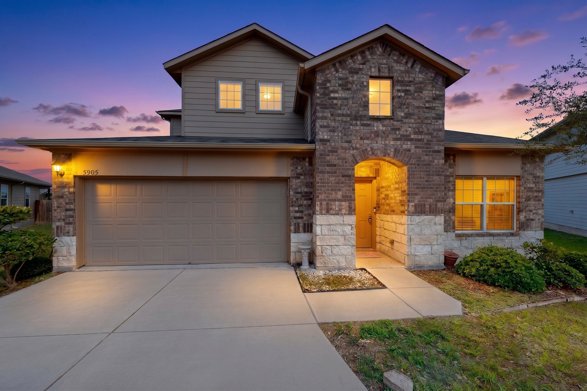 5905 Diamondleaf Bend Austin, TX 78724 - Photo 1 of 38 Two-story facade featuring brick and stone masonry, a two-car garage, and an arched entry with a covered porch