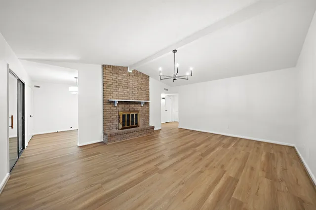 an empty room with wooden floor fireplace and kitchen view