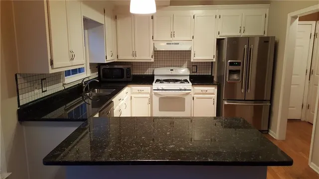 a kitchen with stainless steel appliances granite countertop a refrigerator a stove a sink and white cabinets