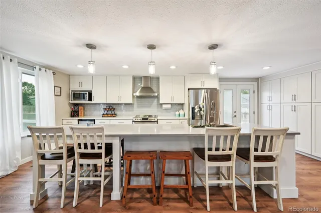 a kitchen with stainless steel appliances kitchen island granite countertop a dining table chairs and white cabinets