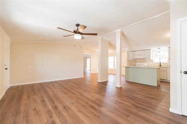 a view of an empty room with wooden floor and a kitchen