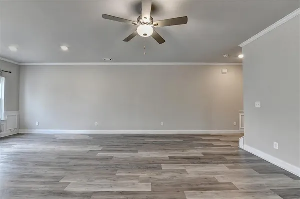 a view of an empty room with wooden floor and a ceiling fan