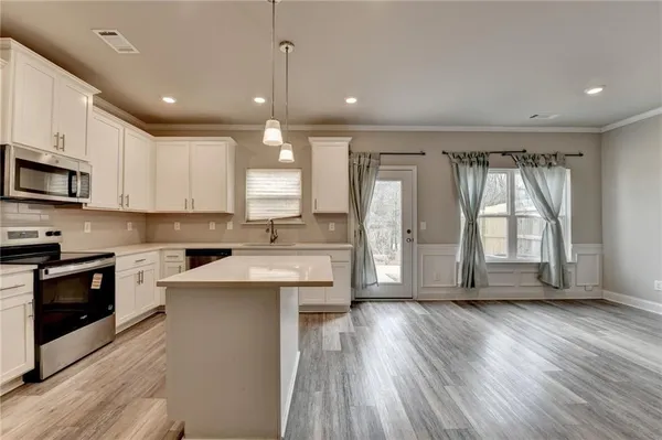 a large kitchen with stainless steel appliances granite countertop a stove a sink a refrigerator and white cabinets with wooden floor