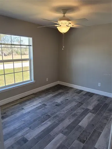 an empty room with wooden floor fan and windows