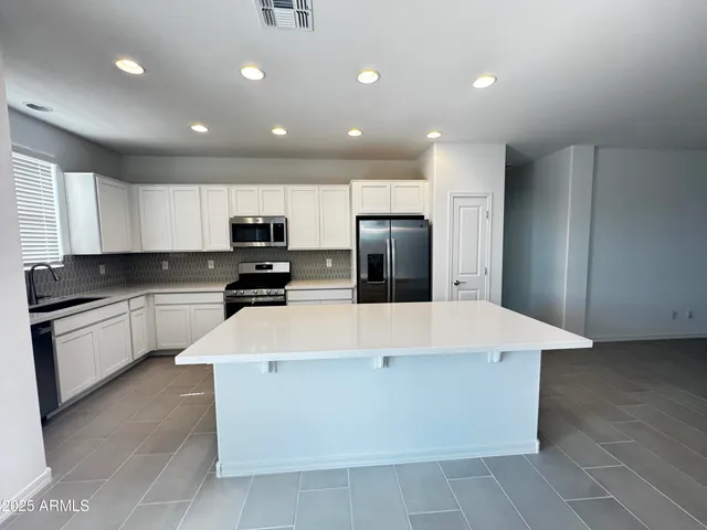 a large kitchen with stainless steel appliances kitchen island granite countertop a refrigerator a sink a stove a microwave and island