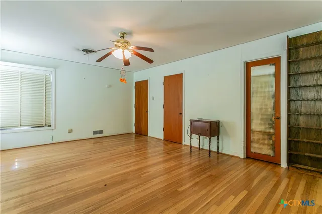 an empty room with wooden floor chandelier fan and windows