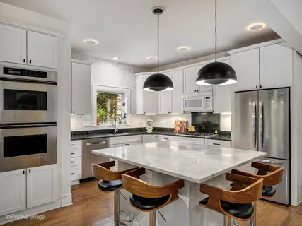 a kitchen with stainless steel appliances a stove a microwave a refrigerator a stove and white cabinets with wooden floor