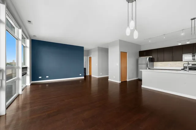 a view of an empty room with wooden floor and a kitchen