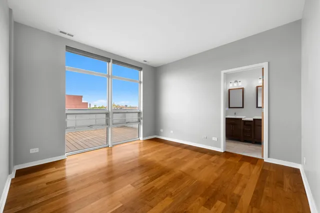 an empty room with wooden floor and way to kitchen