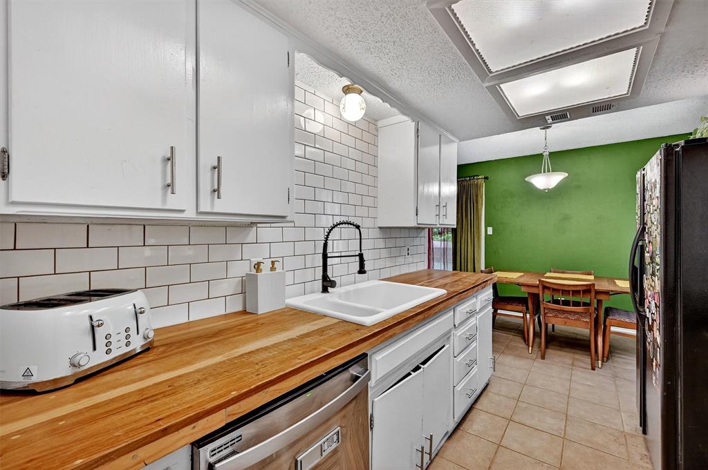 813 Glen Key Street Denison, TX 75020 - Photo 10 of 28 Kitchen with butcher block countertops, freestanding refrigerator, stainless steel dishwasher, decorative backsplash, and a textured ceiling