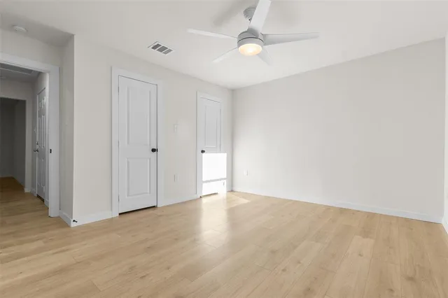 an empty room with wooden floor fan and windows