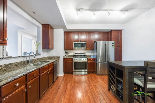 a kitchen with stainless steel appliances granite countertop a refrigerator a sink dishwasher a stove and white countertops with wooden floor