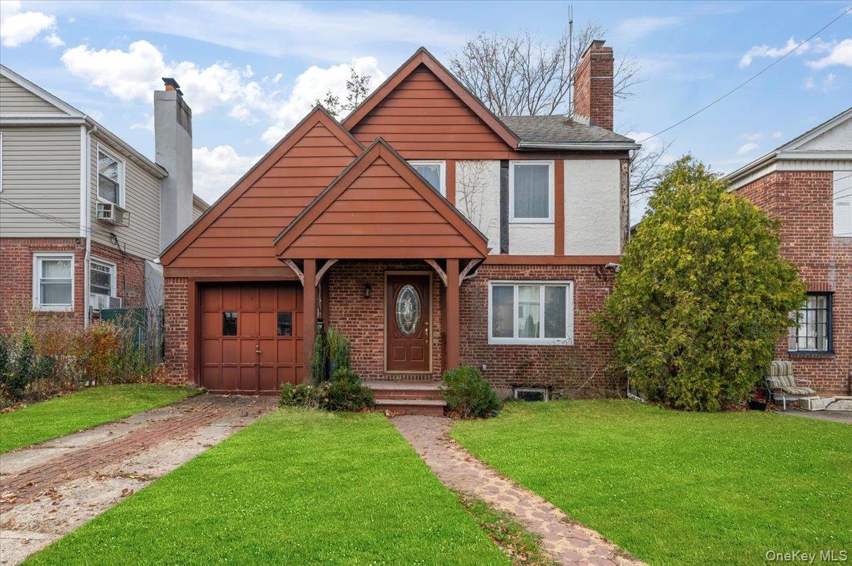 View of front of home with brick siding, a front yard, driveway, and a chimney