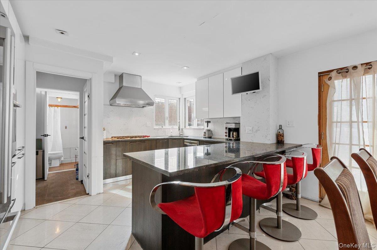 82-06 166th Street Queens, NY 11432 - Photo 4 of 25 Kitchen with a peninsula, light tile patterned flooring, ventilation hood, a kitchen bar, and dark stone countertops