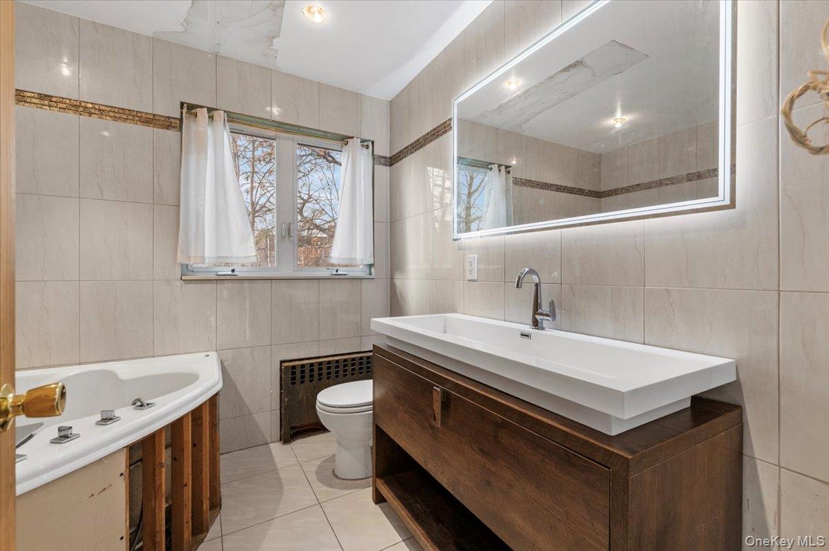 82-06 166th Street Queens, NY 11432 - Photo 10 of 25 Bathroom featuring vanity, radiator heating unit, a garden tub, tile walls, and light tile patterned floors