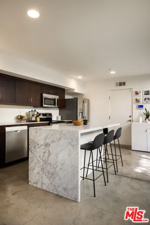 a kitchen with stainless steel appliances kitchen island granite countertop a refrigerator a stove a sink a dining table and chairs with wooden floor