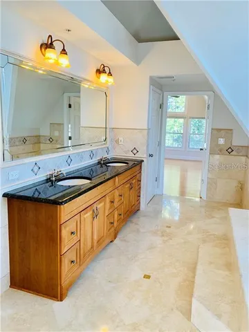a spacious bathroom with a granite countertop double vanity sink a mirror and a bathtub