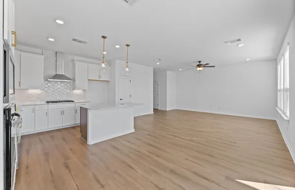 a view of an empty room with wooden floor and a kitchen