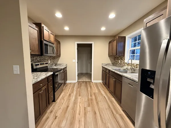 a kitchen with stainless steel appliances granite countertop a refrigerator a stove top oven a sink dishwasher and wooden floor